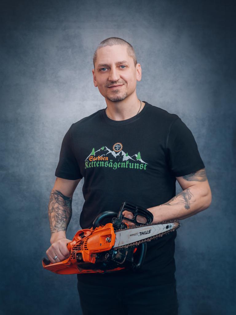 Porträt von Andreas Patzak mit einer Motorsäge vor neutralem Hintergrund für die Einrichtung Sachsen Kettensägenkunst.