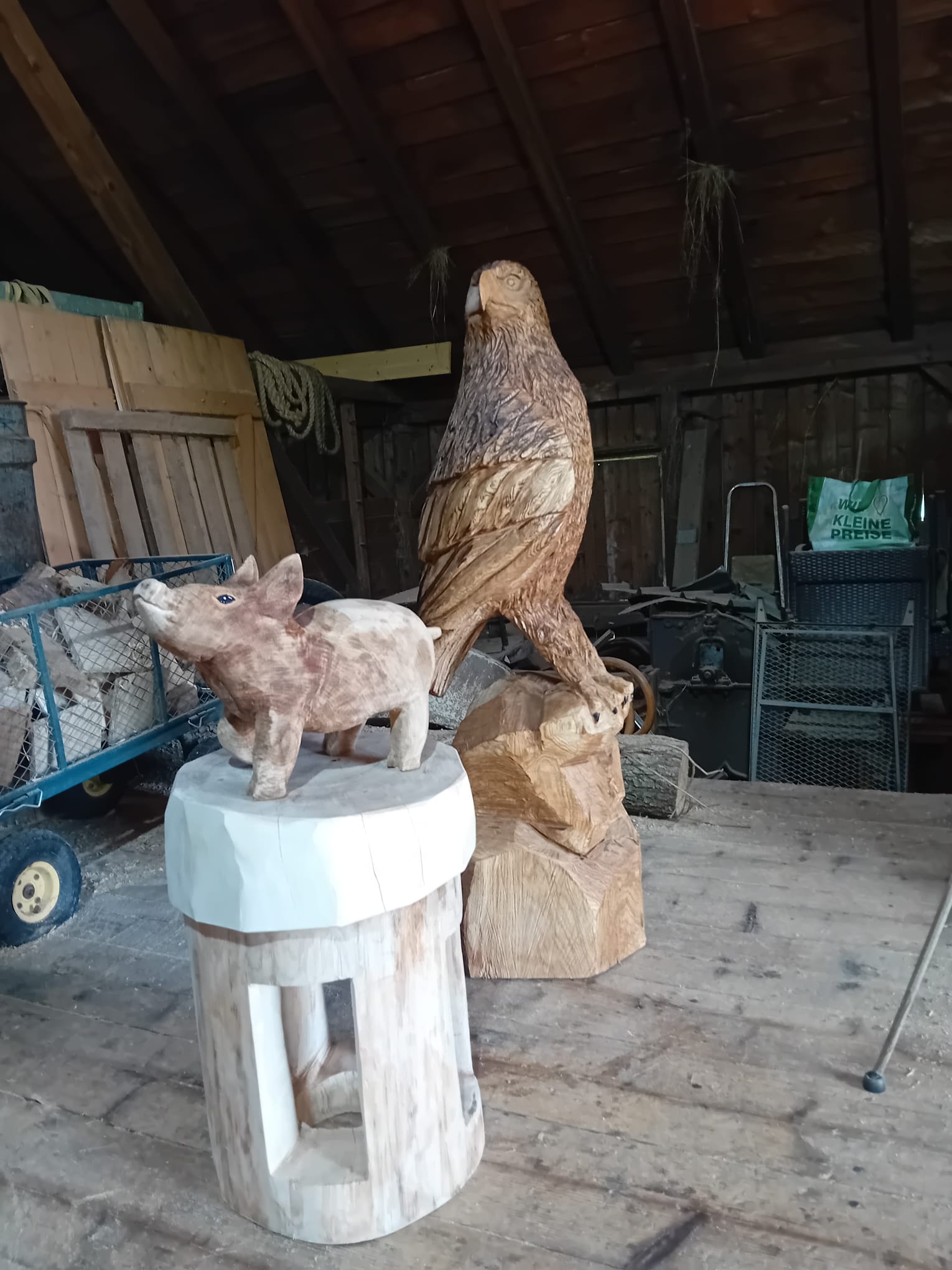 Eine große Adlerfigur und ein kleineres Schwein aus Holz in der Werkstatt von holzskulpturen.com.