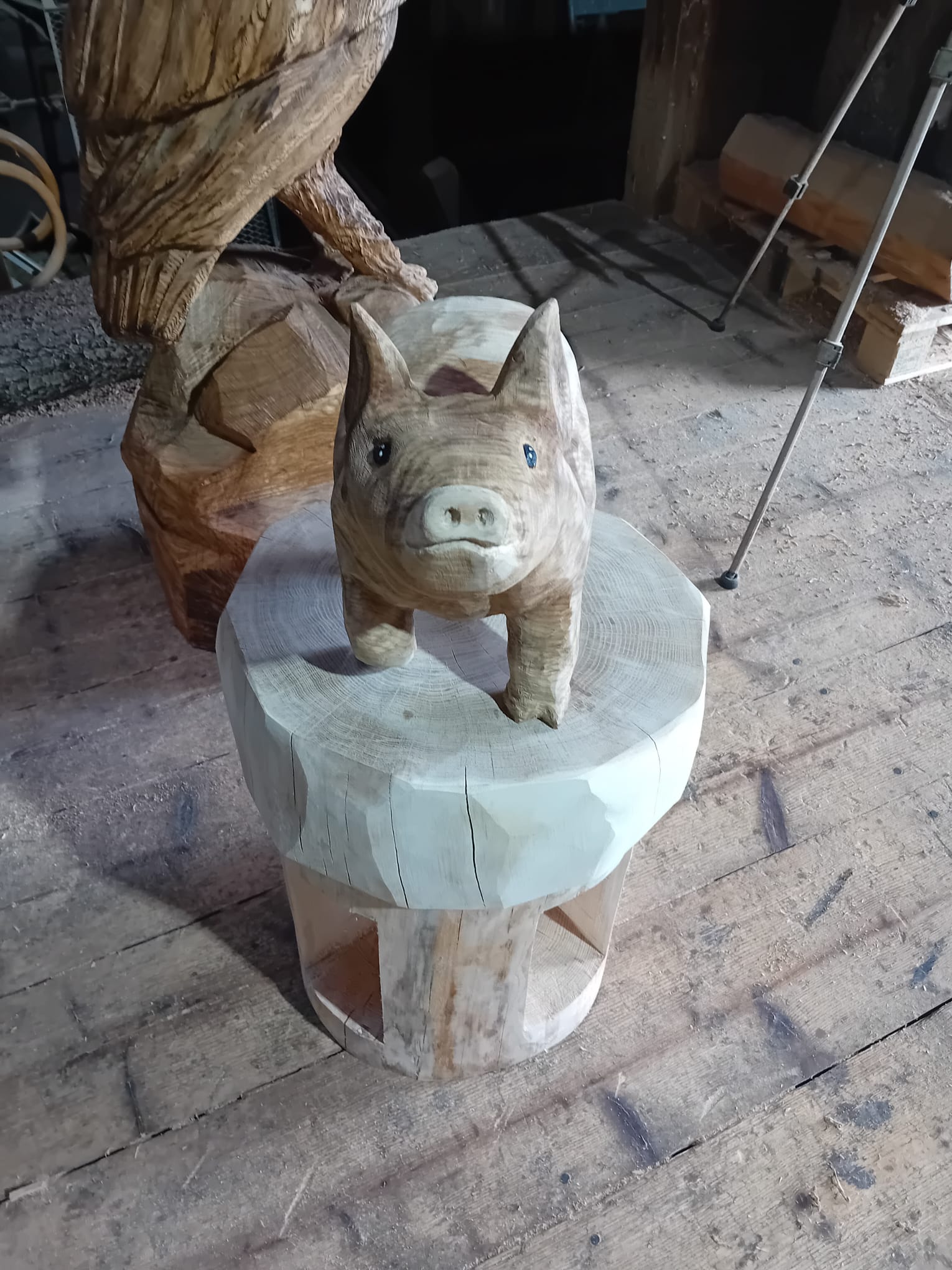 Eine rustikale Holzskulptur in Form eines Schweins auf einem Holzsockel in der Werkstatt von Holzskulpturen.com.