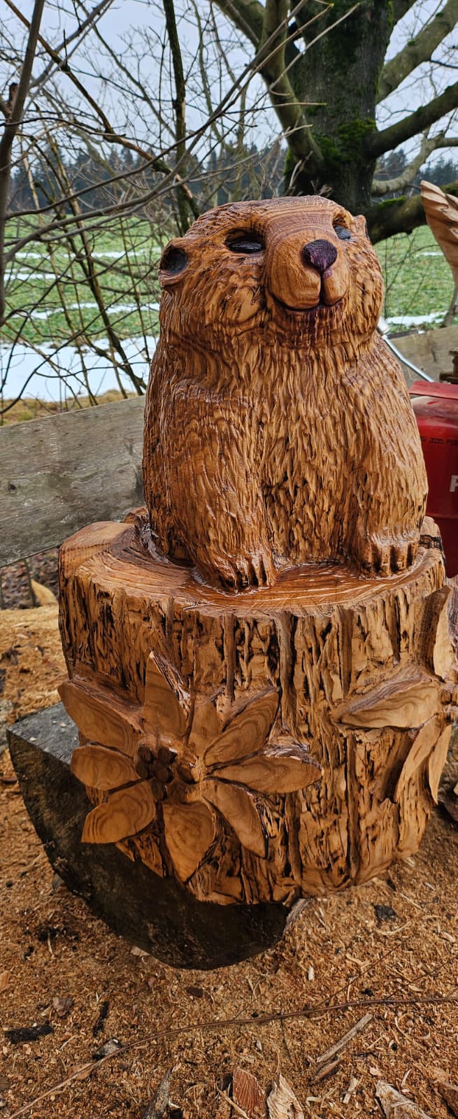 Holzgeschnitztes Murmeltier auf einem Baumstamm mit Blumenverzierung im Außenbereich von Andreas Patzak